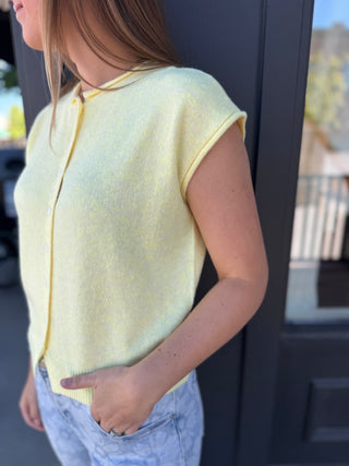 Person wearing a yellow sleeveless sweater with a blurred background
