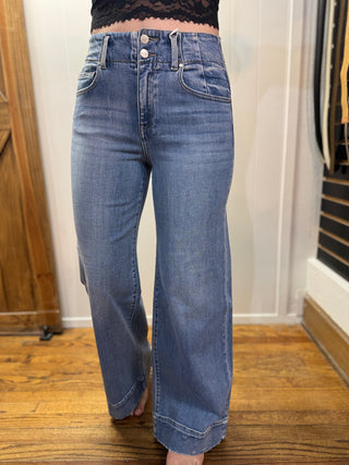 Person wearing blue jeans standing on a wooden floor with a white wall background
