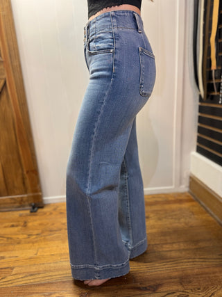 Person wearing blue jeans standing in a room with wooden floor and white walls.