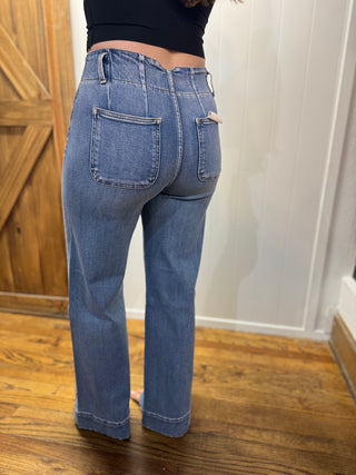 Person wearing blue jeans standing on a wooden floor with a white wall in the background