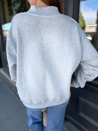 Person wearing a light gray sweater and blue jeans standing by a door.