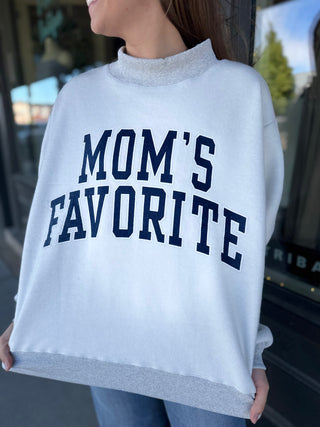 White sweatshirt with 'MOM'S FAVORITE' text worn by a person, blurred background