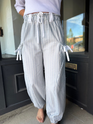 Person wearing blue and white striped pants with drawstring waist, standing in a room.