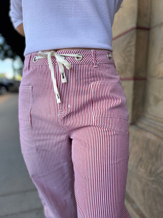 Red and white striped pants with a white drawstring worn by a person, against a blurred background.