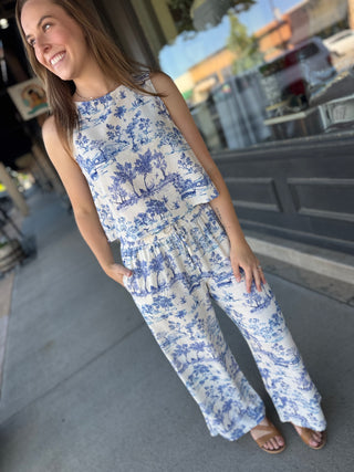 Woman wearing a blue and white floral jumpsuit standing on a sidewalk.