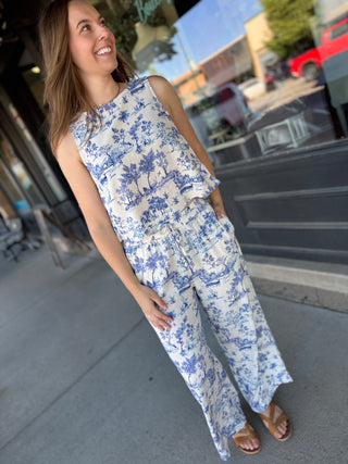 Woman wearing a blue and white floral jumpsuit standing on a sidewalk.