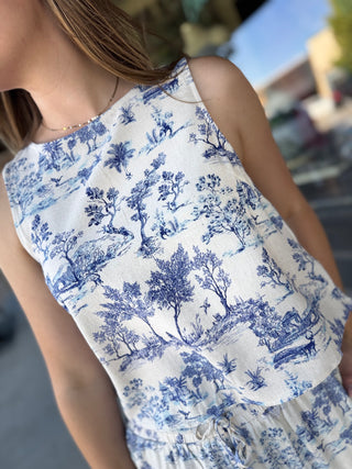 Person wearing a sleeveless dress with blue floral pattern in an outdoor setting