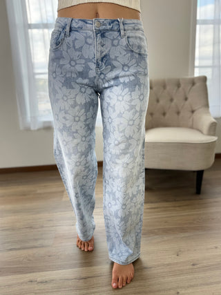 Person wearing light blue floral jeans standing in a room with a couch and windows.