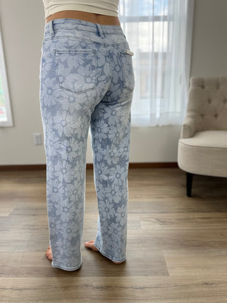 Person wearing light blue floral jeans standing in a room with a couch and window.
