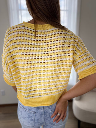 Person wearing a yellow and white striped sweater in a room with neutral decor.