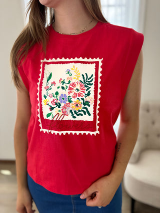 Person wearing a red sleeveless shirt with floral embroidery design.
