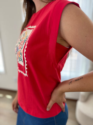 Person wearing a red sleeveless top with a colorful design on a blurred indoor background