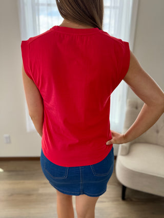 Person wearing a red sleeveless top and blue shorts indoors.