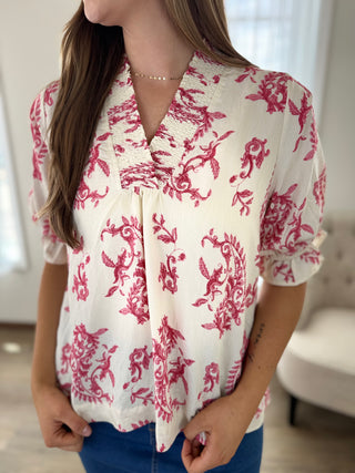 Woman wearing a white blouse with red floral patterns in a blurred indoor setting