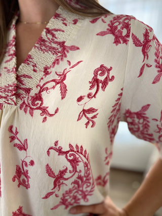 Close-up of a person wearing a white blouse with red floral patterns.