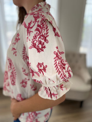 Person wearing a white blouse with red floral patterns in a blurred indoor setting