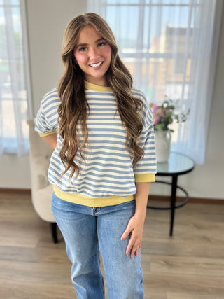 Lady standing wearing a stripe  knit top with banded sleeves and bottom.