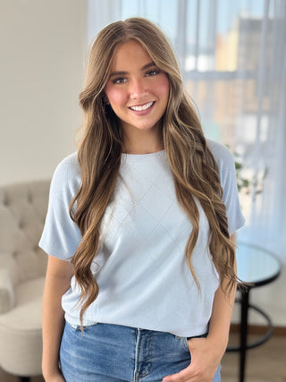 Lady standing wearing a baby blue knit sweater.