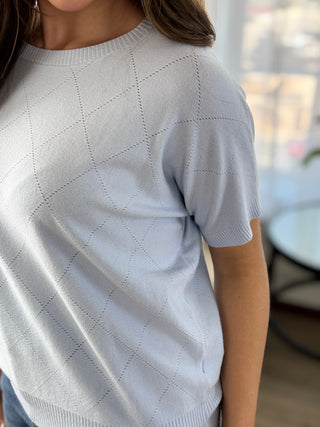 Lady standing wearing a baby blue knit sweater.