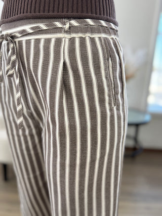 Close-up of a person wearing striped trousers with a matching tie belt, paired with a dark brown ribbed top. The pants feature vertical stripes in brown and off-white.