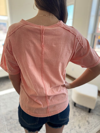 Lady standing wearing peach washed tee with front pocket and denim shorts.