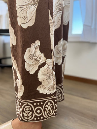 Close-up of a person wearing brown wide-leg pants with a cream floral and border print, standing on a wooden floor in an indoor room.