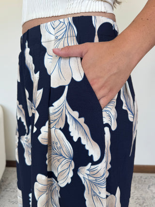 Close-up of a person wearing navy blue wide-leg pants with a large cream floral print, showing a hand in the side pocket.