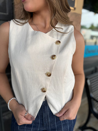 A woman wearing a sleeveless cream-colored linen vest with brown buttons, paired with dark blue pinstriped pants.