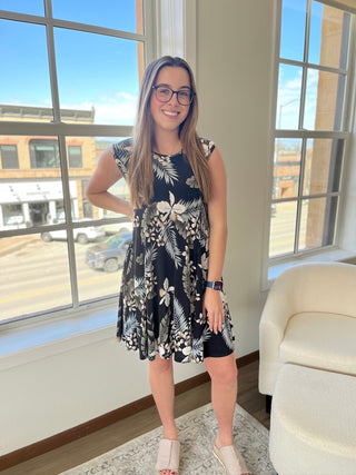 A photo of a girl in a tropical patterned dress standing in front of a window.