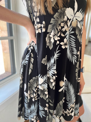 A photo of a girl in a tropical patterned dress standing in front of a window.