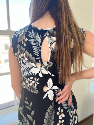 A photo of a girl in a tropical patterned dress standing in front of a window.