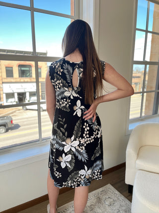 A photo of a girl in a tropical patterned dress standing in front of a window.