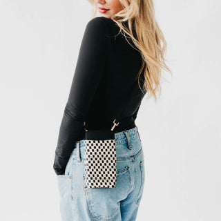 Person wearing a black long-sleeve top and blue jeans with a checkered waist bag on a white background