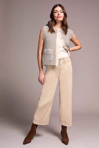Woman wearing a sleeveless checkered vest, white shirt, beige pants, and brown shoes on a plain background