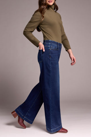 Woman wearing a green turtleneck and blue jeans on a gray background
